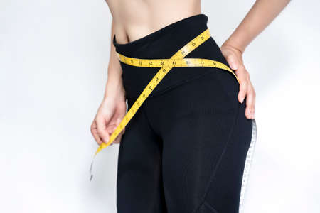 A skinny woman wearing black pants uses a tape measure around her waistline against with white background. Health care concept.の写真素材