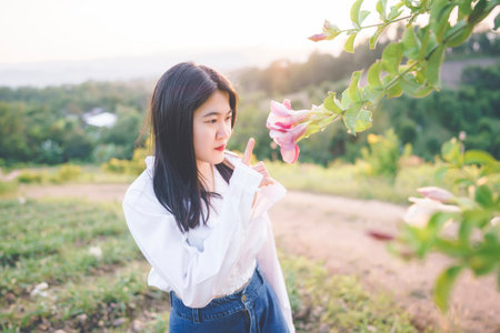 A woman in a white shirt pointing to a beautiful pink flower in a garden with a view of nature.の写真素材