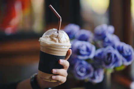 Man's hand holding a glass of smoothie with floral background in a cafe