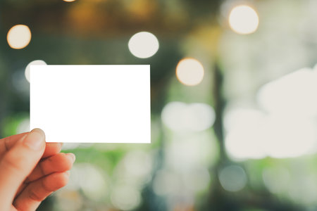 Woman's hand holding a small blank white paper with bokeh background.の写真素材