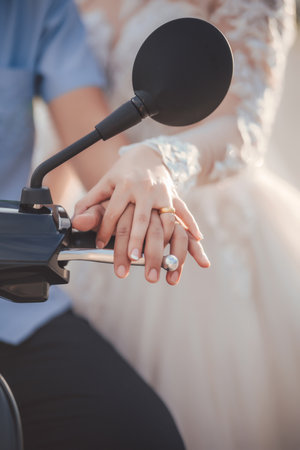 The clasped hands of a couple wearing wedding rings on the handlebars of a motorcycle. Wedding concept.の写真素材