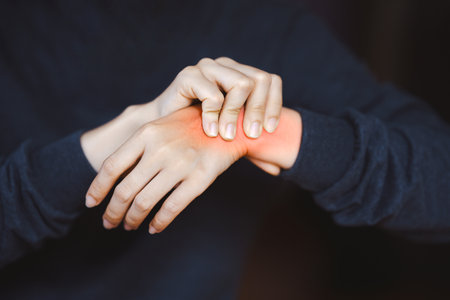 Person holding wrist with visible pain or inflammation, indicating injury or discomfort, on a dark background. Concept of pain or health issues.の写真素材