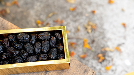 A golden box filled with Dried ajwa dates, placed on a wooden surface with scattered autumn leaves in the background.の写真素材