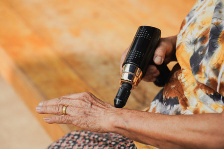 A close-up of an elderly person using a modern massage device on their hand, showcasing relaxation techniques and self-care practices in a serene environment.の写真素材
