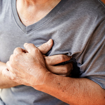 elderly person in gray shirt clutches their chest, possibly indicating discomfort or pain. image conveys sense of urgency and concern.の写真素材