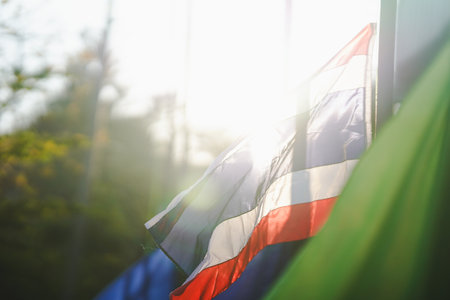 A vibrant Thai Flag waves gently in the sunlight, showcasing bright colors against a blurred natural...