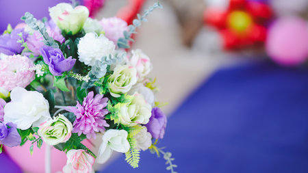 A vibrant arrangement of artificial flowers in shades of purple, white, and green, set against a soft, colorful background.の写真素材