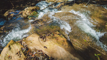 A clear stream flows over rocky terrain, creating ripples and showcasing the natural beauty of the surrounding environment, in Tak Thailand.の写真素材