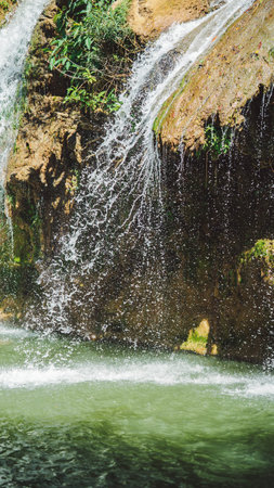 A serene waterfall cascades over rocky terrain into a tranquil pool, surrounded by lush greenery, creating a peaceful natural scene, in Tak Thailand.の写真素材