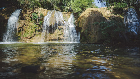 A serene waterfall cascading into a clear pool, surrounded by lush greenery and rocky formations, in Tak Thailand.の写真素材