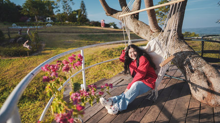 A woman relaxes on a swing in a scenic outdoor setting, surrounded by flowers and nature, enjoying a peaceful moment.の写真素材