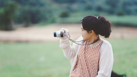 A young woman takes a photo with a camera in a lush green landscape, showcasing her passion for...