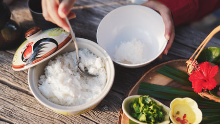 A bowl of rice is being served, accompanied by fresh herbs and vibrant garnishes, set against a rustic wooden backdrop.の写真素材
