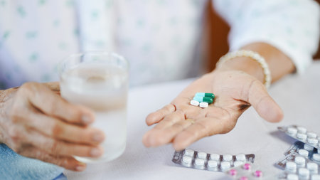 An elderly hand holding pills, tablets, and capsules with glass of water, medication, healthcare, close upの写真素材
