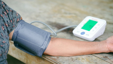 Close up of elderly person measuring blood pressure with digital sphygmomanometer on wooden table during health check at home.の写真素材