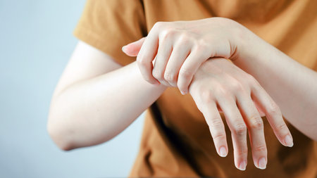 A person in brown shirt gently holds their wrist with opposite hand, possibly indicating pain,...