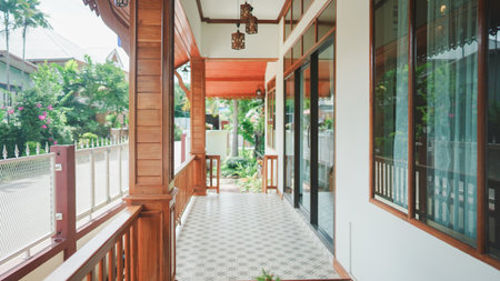 A traditional Thai-style wooden porch with tiled floor and garden view, showing warm tropical residential architecture.の写真素材