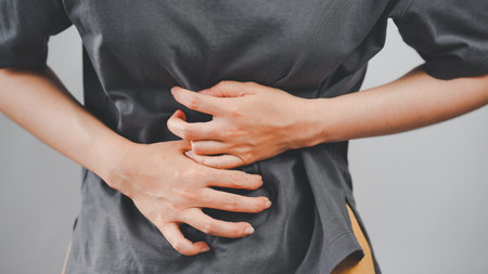 Close-up of a woman clutching her stomach with both hands, depicting abdominal pain or discomfort,...