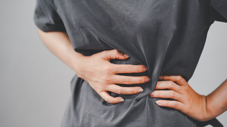 Close-up of a woman holding her side in pain, indicating stomach cramps or abdominal discomfort, ideal for health, medical, and wellness content.の写真素材
