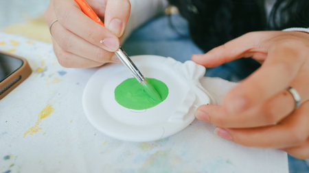 Close-up of hands painting green color on a plaster art piece using a brush, suitable for arts, crafts, and DIY concept.の写真素材