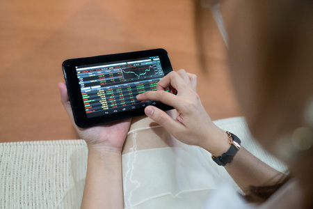Hands of Asian woman using her tablet to check the stock market on the screen with numbers and graph.の写真素材