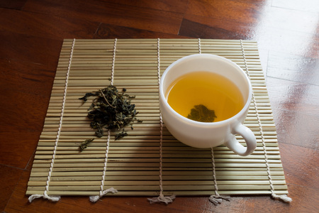 Cup of clear yellow tea and dried tea leaves on a small bamboo mat.の写真素材