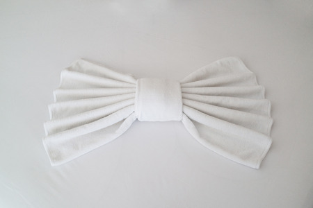 White towels folded into a bow shape lying on the white bed sheet.の写真素材