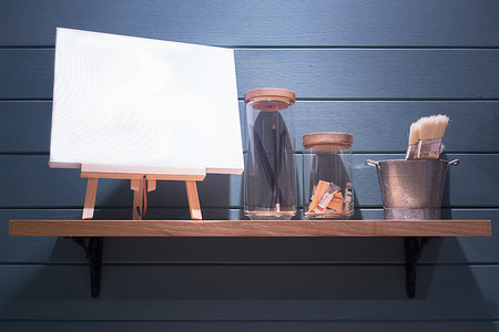 Blank canvas on the shelf with paint brushes in the bucket and pencils in the jar.の写真素材