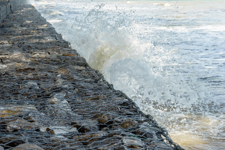 Sea Waves crash into long stone seawall along shoreline.の写真素材