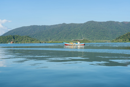 Small red wooden boat on water with green mountain and blue sky background.の写真素材