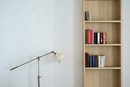 Metal lamp stand and wooden bookshelf with colorful books on white wallの写真素材