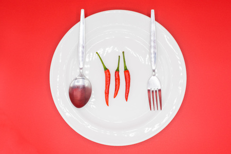 Top view of red chillies on white plate with cutlery and red background.の写真素材