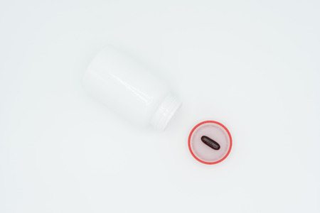 Black capsule on red cap and open white bottle on white background.の写真素材