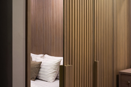 Pattern of wooden closet in bedroom with white pillows and bed.