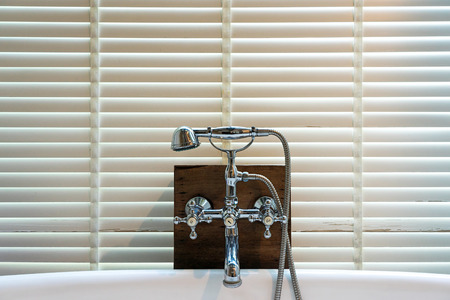 Steel faucets and shower head on wooden board with white wooden chick curtain background.