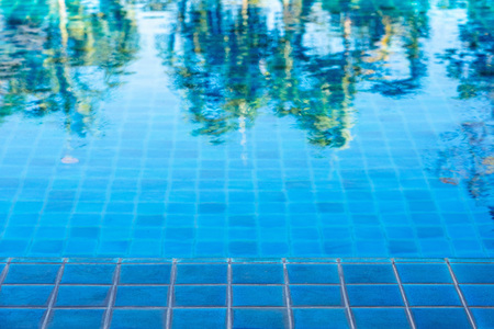 Abstract of green trees reflection on swimming pool with blue mosaic tiles.