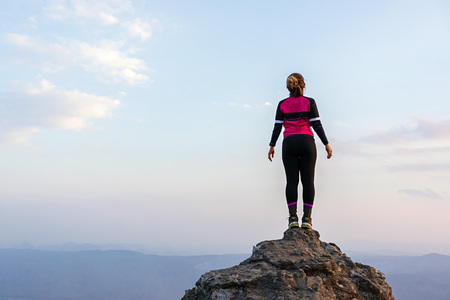 Asian woman in sportswear standing on high rock cliff with horizon over land and sky in the background.の写真素材