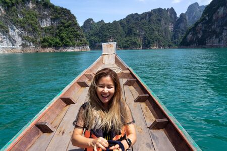 Asian woman laughing on wooden boat in the lake with limestone mountains in the background at...