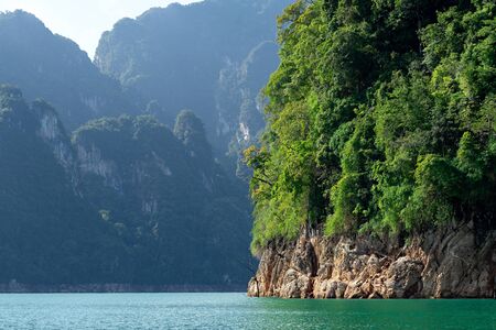 Green trees on rocky island with limestone mountain range and lake in Khao Sok National Park in...