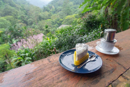 Piece of cake on blue plate and drink in white cup with green forest background in Chiang Mai,...