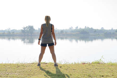 Asian female back in sportswear standing sweaty with white lake and sky background in Thailand.