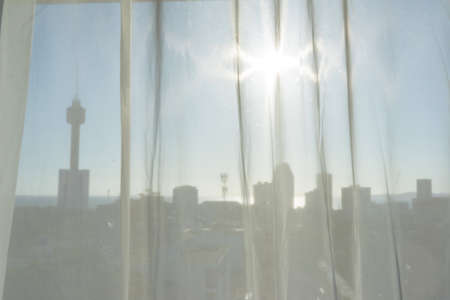 Blurry abstract silhouette of Pattaya city with shining sun through soft white curtain.
