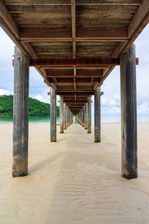 View under a wooden pier on sand beach with sea and cloudy sky background on Koh Kood island in Trat, Thailandの写真素材