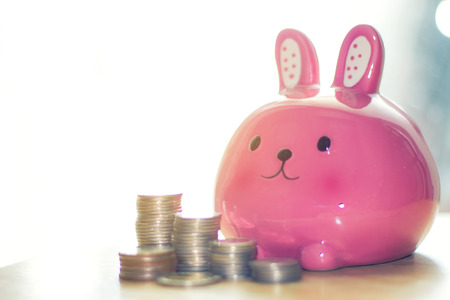 Pink rabbit bank and coins on wooden table,Concept saving money for future use