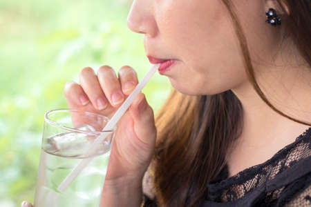 The womandrinks clean  water from a glass through a strawの写真素材