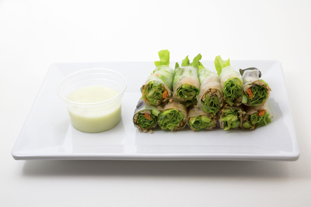 Portion of tuna salad spring rolls with Vasabi sauce, vegetables and in noodle tube on white backgroundの写真素材