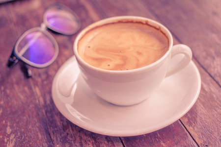 A cup of coffee latte on wooden table with a pair of glassesの写真素材