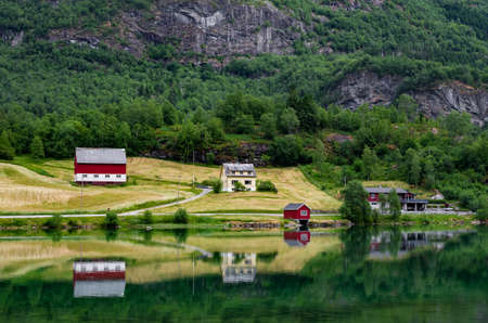 Beautiful Norwegian landscape reflected in mirror like water surface of a lake. Farm houses, forest,...