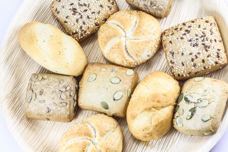 Breads and buns assortment on palm leaf plate on white background