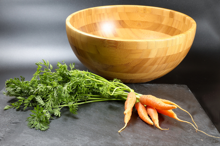 Small baby carrot with green leafs wooden bowl black backgroundの写真素材